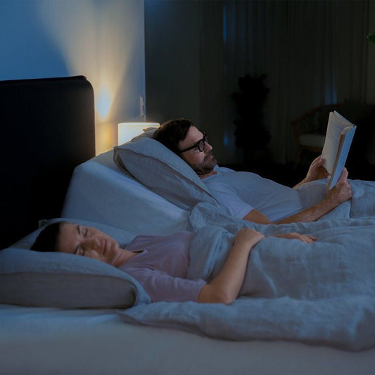 Couple relaxing in bed with ergonomic Vitasova pillow, reading before sleep for improved rest and spine support